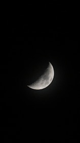 A crescent moon is visible against a deep black sky, with detailed craters and surface textures highlighted by the light.