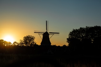 A vibrant sunset over the plains of Castilla-La Mancha with windmills silhouetted against the sky.