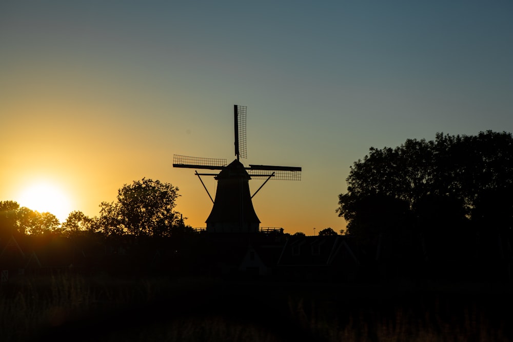 a windmill is silhouetted against the setting sun