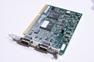 A green circuit board with multiple integrated circuits and electronic components, including resistors, capacitors, and connectors. The board features a series of gold-plated connectors on one edge and various chips labeled with 'Hayes,' indicating it is likely a computer hardware component such as a modem. The surface is populated with detailed white printed traces and black connectors for interfacing.