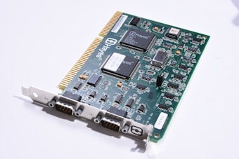 A green circuit board with multiple integrated circuits and electronic components, including resistors, capacitors, and connectors. The board features a series of gold-plated connectors on one edge and various chips labeled with 'Hayes,' indicating it is likely a computer hardware component such as a modem. The surface is populated with detailed white printed traces and black connectors for interfacing.