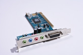 A computer sound card with several colored input/output ports and an array of electronic components, including capacitors and integrated circuits, mounted on a blue circuit board.