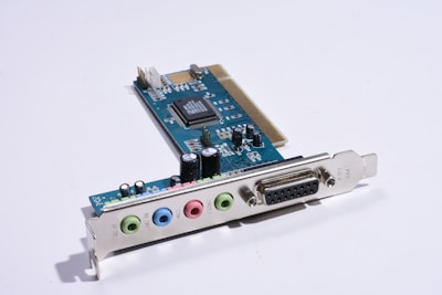 A computer sound card with several colored input/output ports and an array of electronic components, including capacitors and integrated circuits, mounted on a blue circuit board.