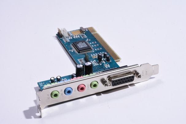 A computer sound card with several colored input/output ports and an array of electronic components, including capacitors and integrated circuits, mounted on a blue circuit board.