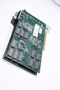 A close-up view of an electronic circuit board featuring various electronic components such as integrated circuits and connectors, mounted on a green printed circuit board. The board has a metallic bracket on one end for mounting in a computer case, and a gold-plated edge connector for interfacing with a computer motherboard.