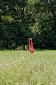 A pair of red sculpture legs are inverted in a lush green field, surrounded by tall grass and dense trees in the background.