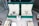 Two luxury watches displayed in elegant green boxes, each marked with the brand's logo. These watches are placed on a soft beige surface within a glass display case, surrounded by other jewelry items including bracelets and watches.