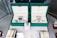 Two luxury watches displayed in elegant green boxes, each marked with the brand's logo. These watches are placed on a soft beige surface within a glass display case, surrounded by other jewelry items including bracelets and watches.