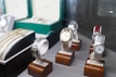 Several luxury watches are displayed on wooden stands, with some showcased in open boxes. The assortment includes different designs and metal finishes, including gold and stainless steel. Bracelets and watchbands are also visible, adding to the luxurious appeal.
