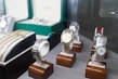 Several luxury watches are displayed on wooden stands, with some showcased in open boxes. The assortment includes different designs and metal finishes, including gold and stainless steel. Bracelets and watchbands are also visible, adding to the luxurious appeal.