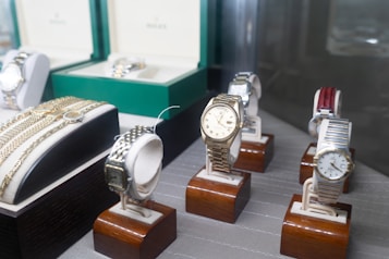 Several luxury watches are displayed on wooden stands, with some showcased in open boxes. The assortment includes different designs and metal finishes, including gold and stainless steel. Bracelets and watchbands are also visible, adding to the luxurious appeal.