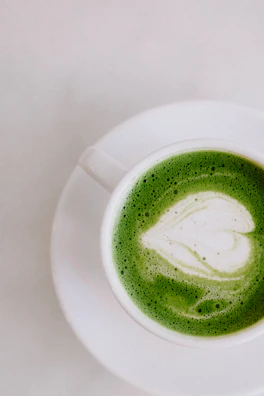 A pastel green ceramic cup filled with frothy matcha latte on a soft pink tablecloth.