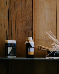 A wooden background provides a rustic setting for a shelf featuring a block of soap and a bottle wrapped with a rustic cap. The items are accompanied by a bowl filled with aromatic sticks, conveying a natural and soothing ambiance.