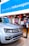 A Volkswagen showroom featuring a silver SUV prominently displayed in the foreground. The background includes a welcoming sign in Portuguese, 'Bem-vindo à Volkswagen,' and various decorations such as red lanterns. The space is well-lit with modern furnishings, and there is a cafe section visible.