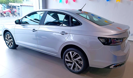 A friendly car dealer showing a customer a sleek sedan from the inventory lot on a sunny day.
