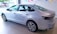 A sleek silver sedan is displayed in a well-lit showroom. The car has a modern design with aerodynamic lines and stylish alloy wheels. The showroom is decorated with colorful triangular flags hanging from the ceiling, adding a festive touch.