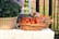 A wicker basket filled with fresh tomatoes and packaged vegetables is placed on a table. Another basket contains leafy greens, possibly kale and green peppers. The setting appears to be outdoors, and a person wearing a striped shirt is partially visible behind the produce.