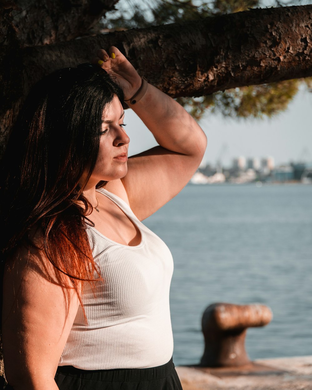 a woman standing next to a tree near the water