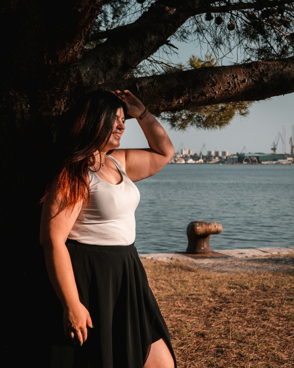 a woman leaning against a tree next to a body of water