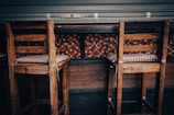 A pair of wooden bar stools with checked cushions are positioned at a high table. The background features a colorful mosaic tile design with a mix of red, orange, and white tiles. The setting appears to be rustic and cozy.