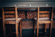 Rustic wooden bar stools with backrests placed around a high wooden table.