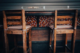 Rustic wooden bar stools with backrests placed around a high wooden table.