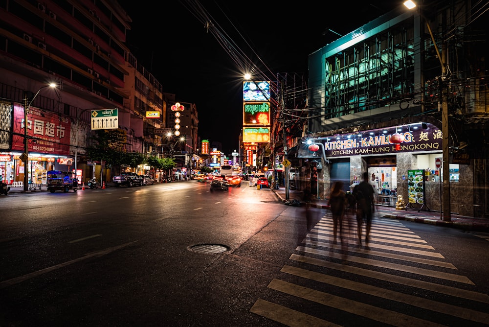 a couple of people walking across a street at night