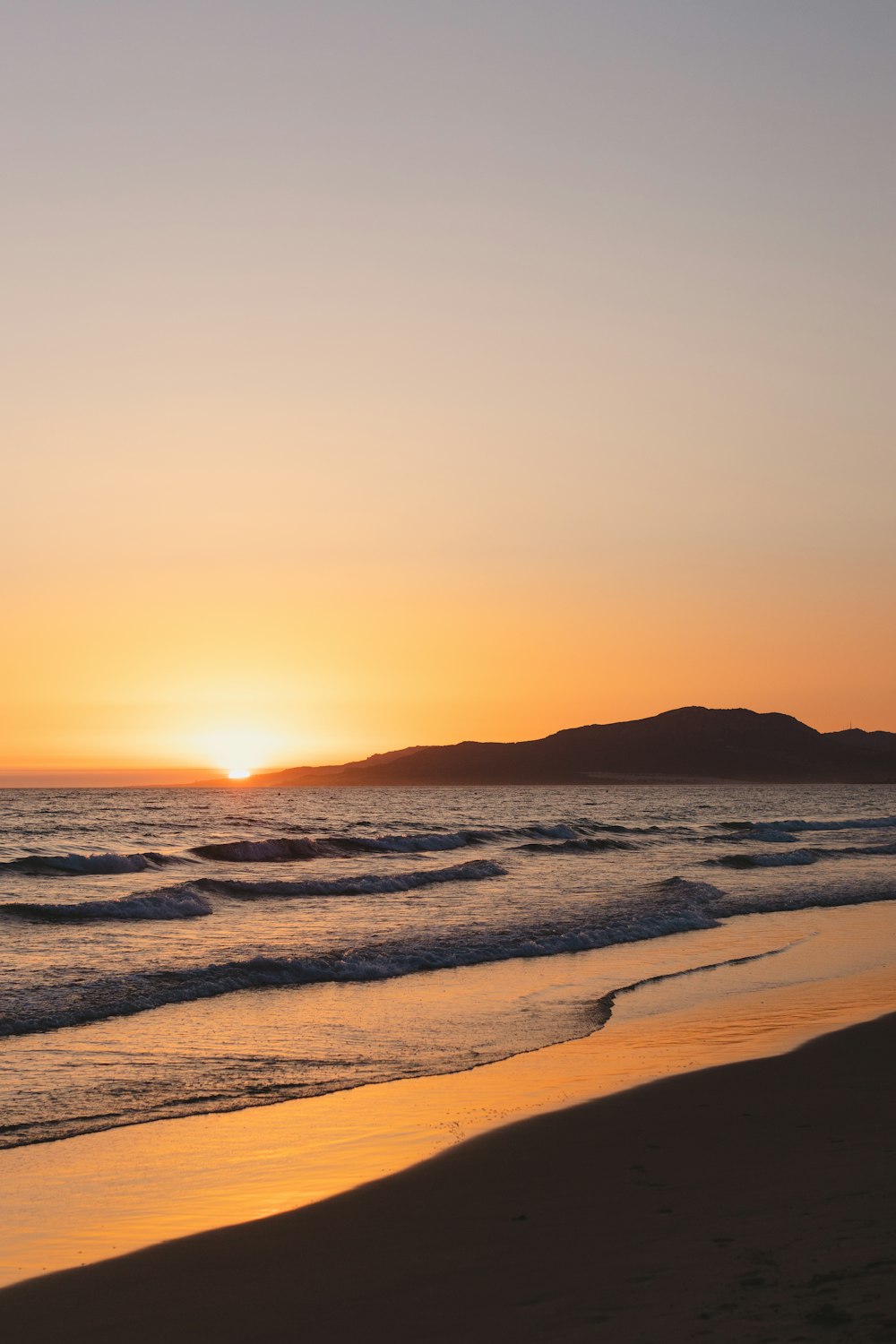 the sun is setting over the ocean on the beach