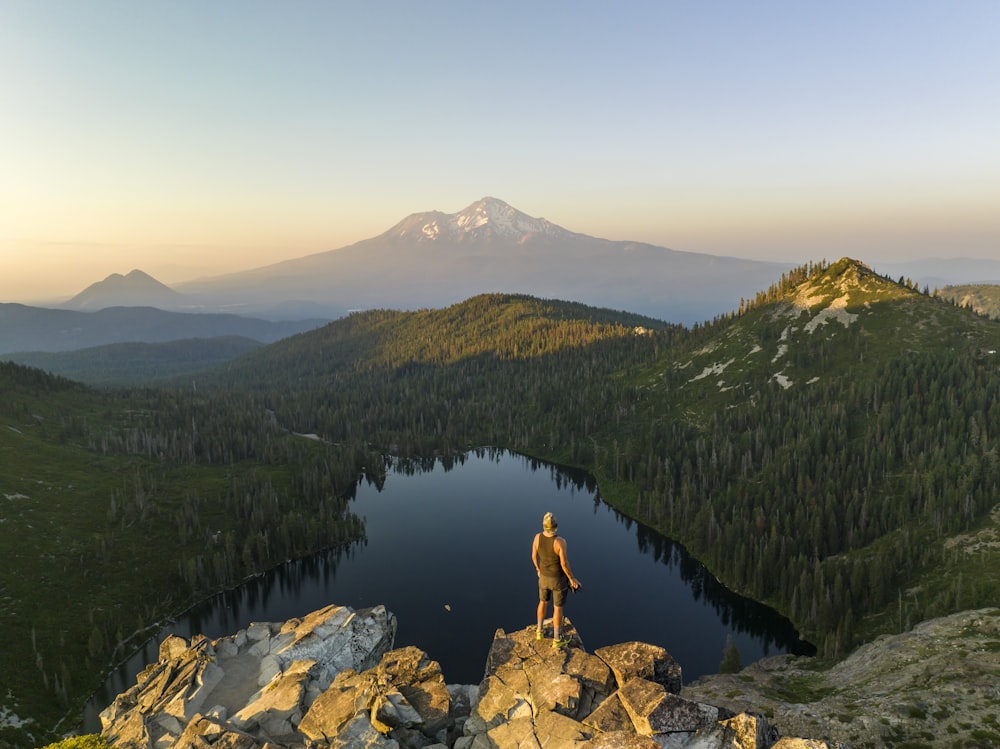 a man standing on top of a mountain next to a lake