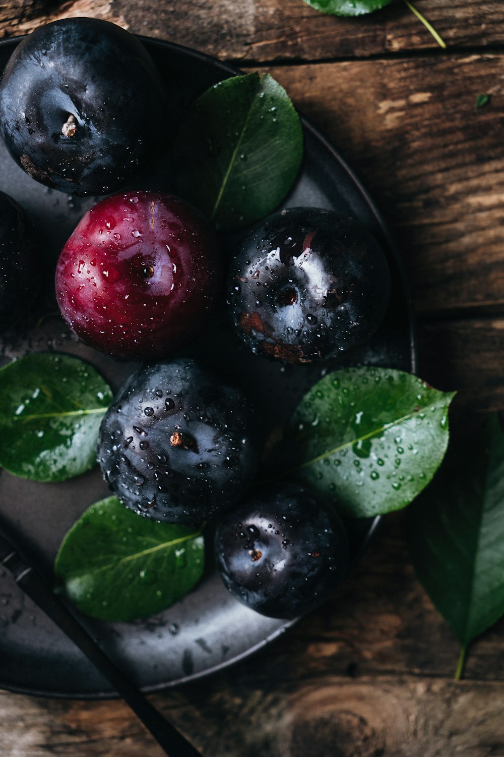 a plate of blueberries with leaves on a wooden table