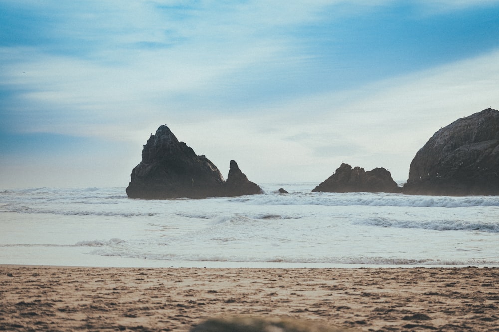 a couple of rocks sitting on top of a sandy beach