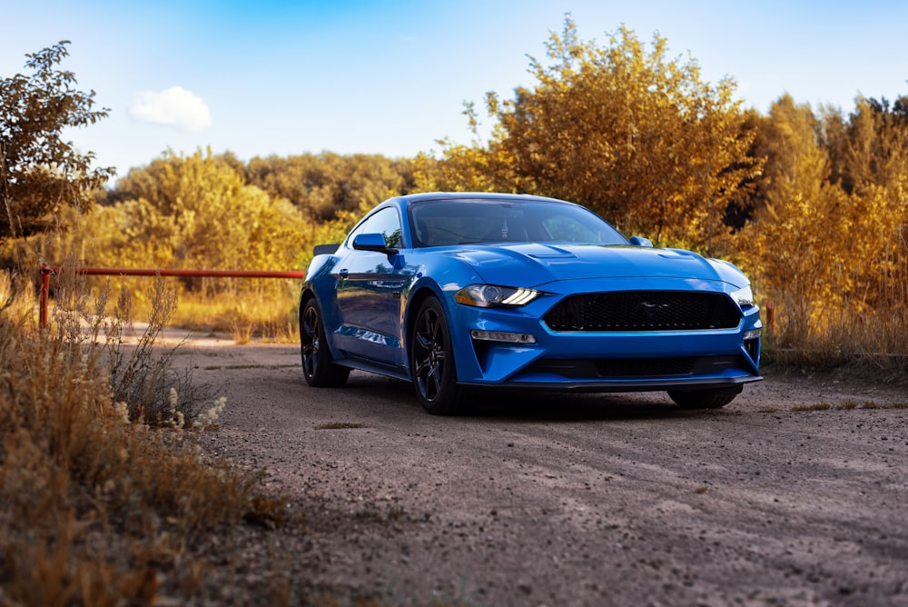 a blue mustang parked on a dirt road