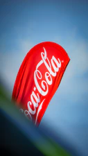 a coca - cola kite is flying in the sky