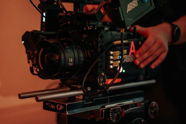 A behind-the-scenes shot of a film set with lighting rigs and a cinematographer adjusting the camera.