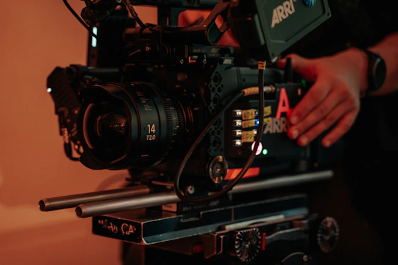 A behind-the-scenes shot of a videographer adjusting a camera lens on a bustling film set.