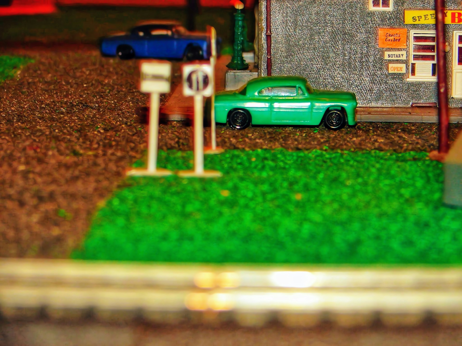Close-up of a detailed 1/64 scale diorama featuring miniature vehicles and buildings under warm lighting