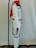 A white costume with black accents, including a black belt, is displayed on a mannequin. The costume has a red scarf draped over the shoulders and is set against a plain background. The mannequin is part of a stand with a visible black base and a metal rod that extends vertically.
