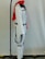 A white costume with black accents, including a black belt, is displayed on a mannequin. The costume has a red scarf draped over the shoulders and is set against a plain background. The mannequin is part of a stand with a visible black base and a metal rod that extends vertically.