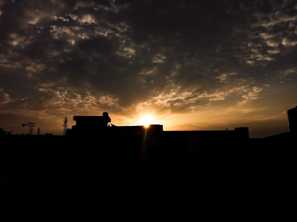 Le soleil se couche derrière un bâtiment au ciel nuageux