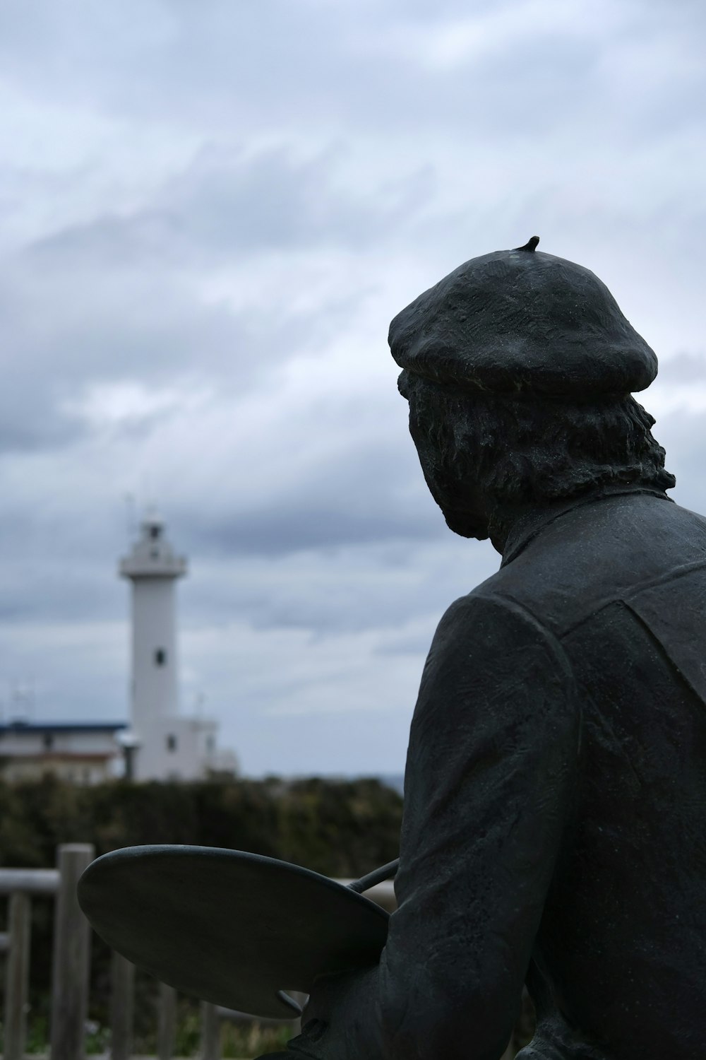 a statue of a man holding a surfboard in front of a lighthouse