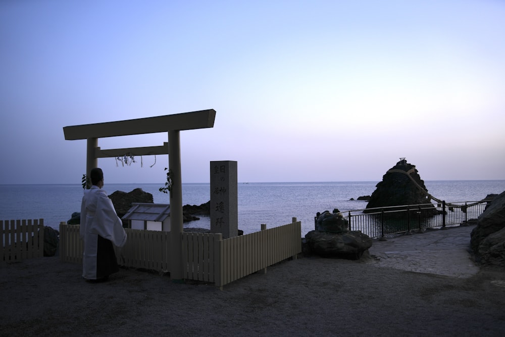 a woman standing next to a wooden structure near the ocean