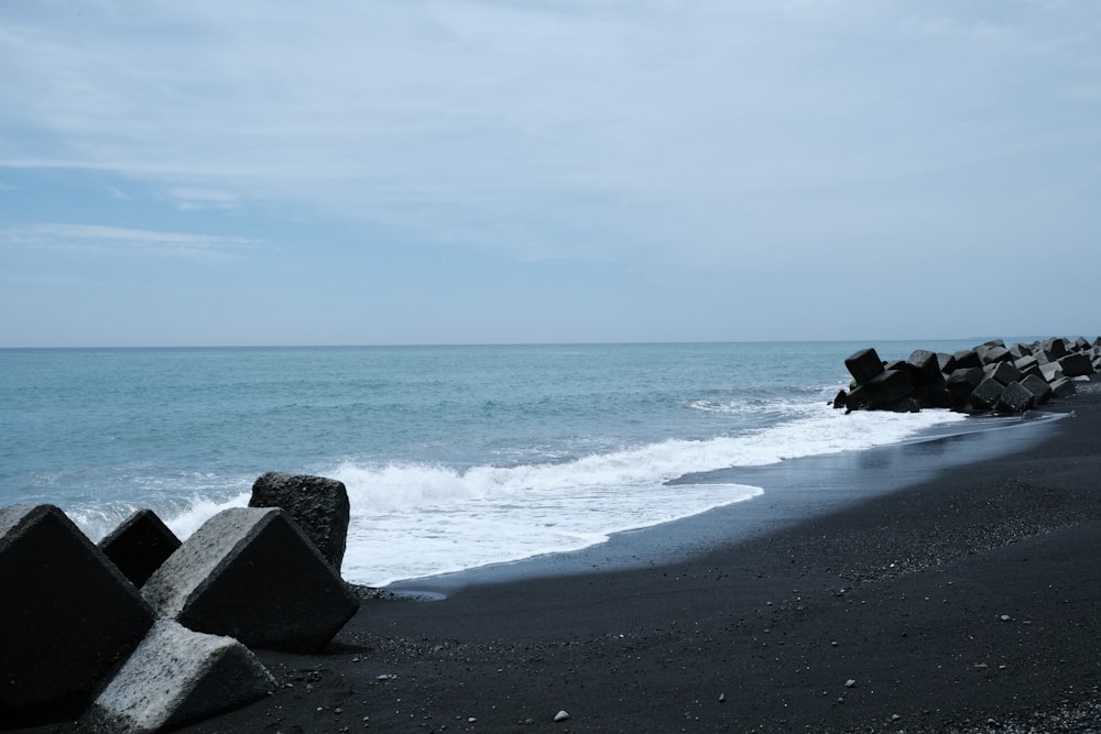 a black beach with rocks and water on a cloudy day