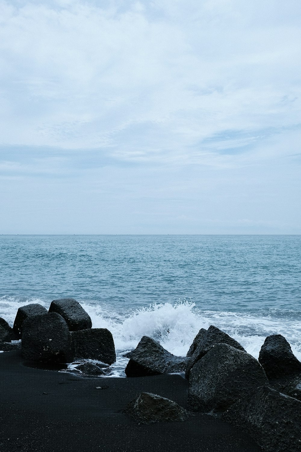 a black sand beach with rocks and a body of water