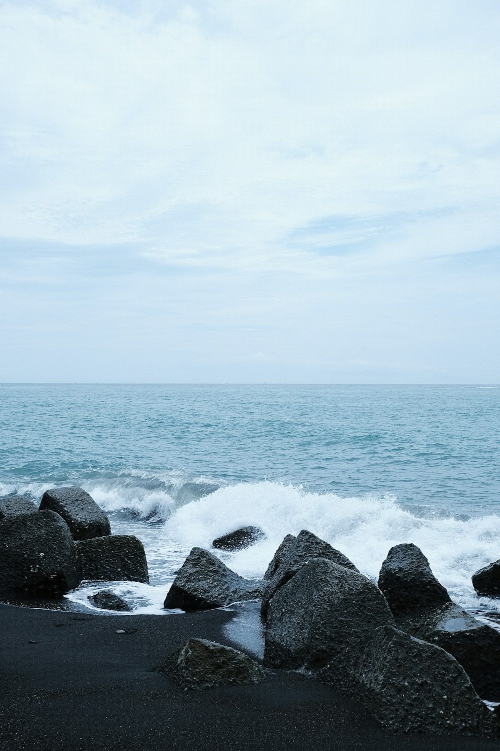 a black sand beach with rocks and a body of water