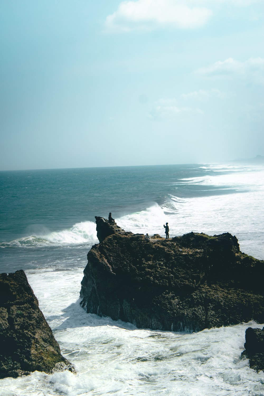 a couple of people standing on top of a rock near the ocean