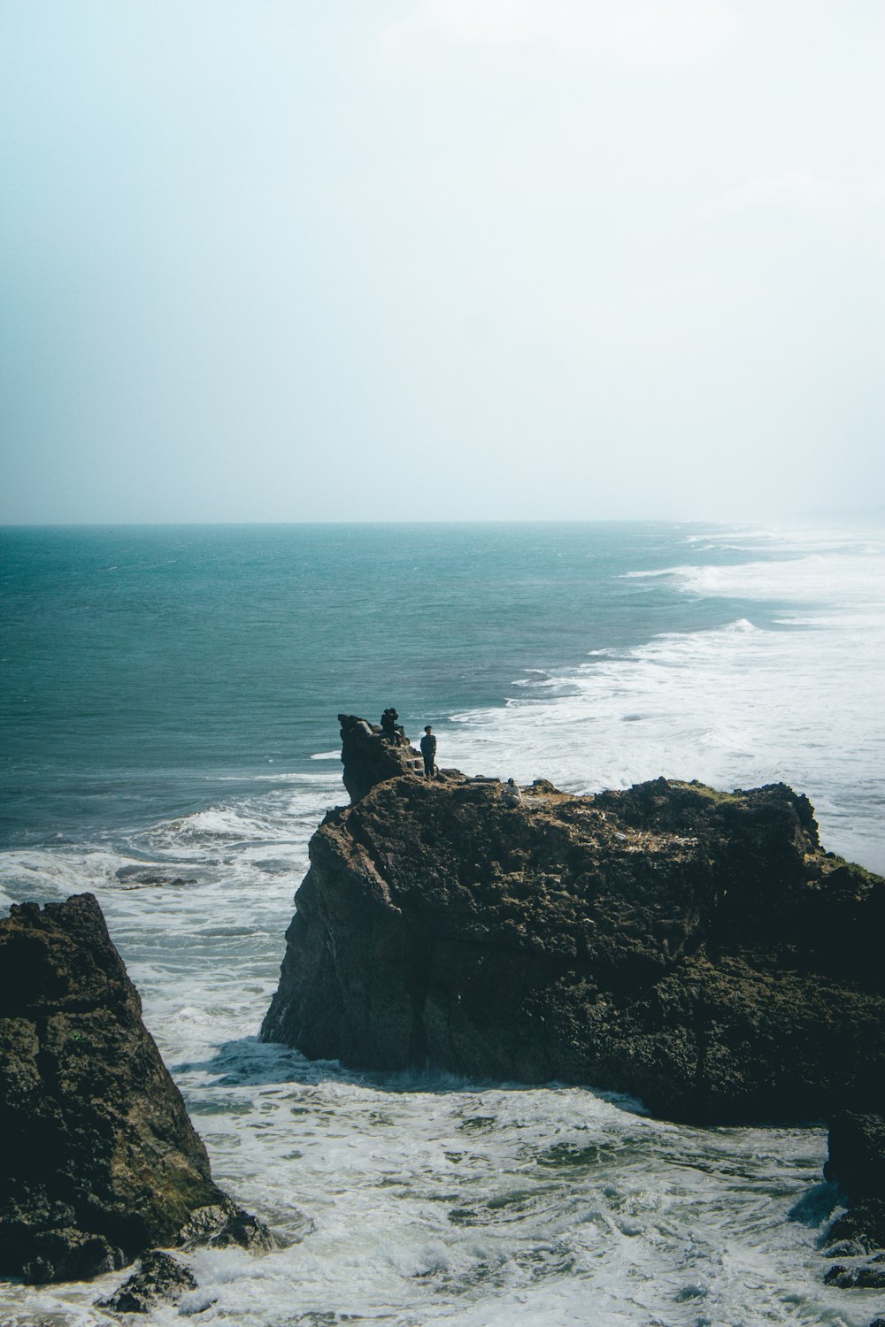 a couple of people sitting on top of a rock near the ocean