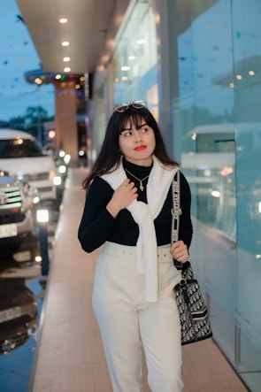 A candid shot of a woman wearing a cream sweater and wide-leg pants, walking through a trendy urban street.