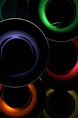 Concentric circles with vibrant neon colors create an abstract and futuristic design. The colors include deep green, blue, red, orange, and yellow, set against a dark background, enhancing the glowing effect.