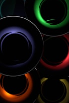 Concentric circles with vibrant neon colors create an abstract and futuristic design. The colors include deep green, blue, red, orange, and yellow, set against a dark background, enhancing the glowing effect.