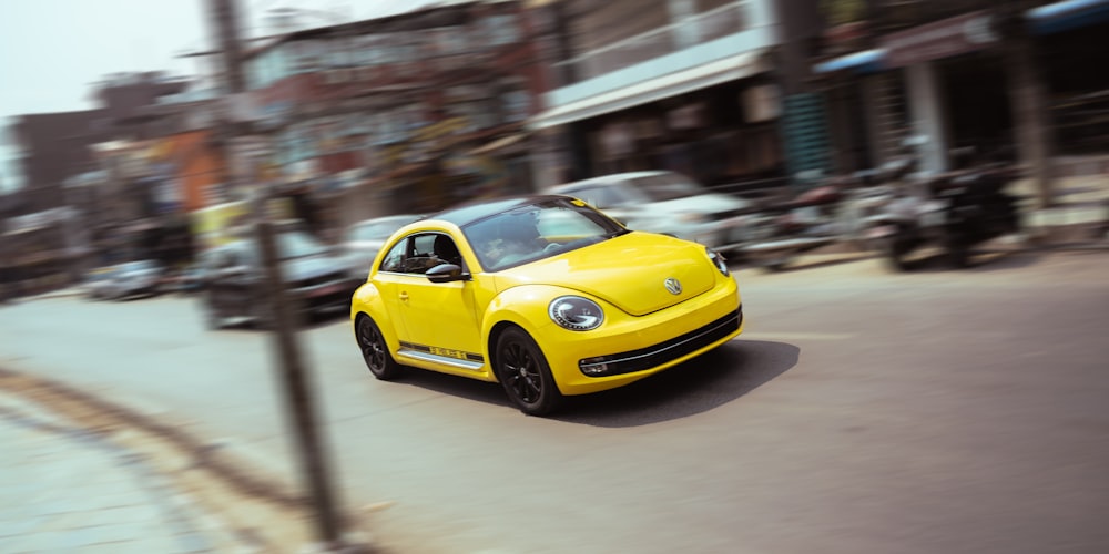 a yellow car driving down a street next to tall buildings